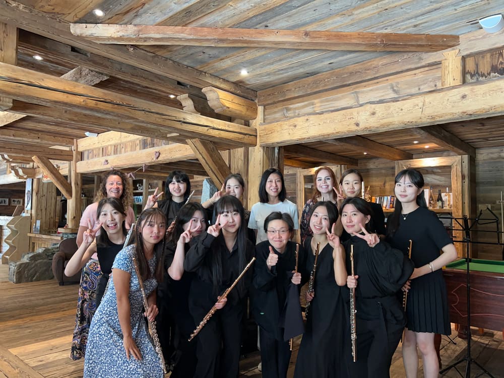 A large group of flutists posing in a timber-beamed hall