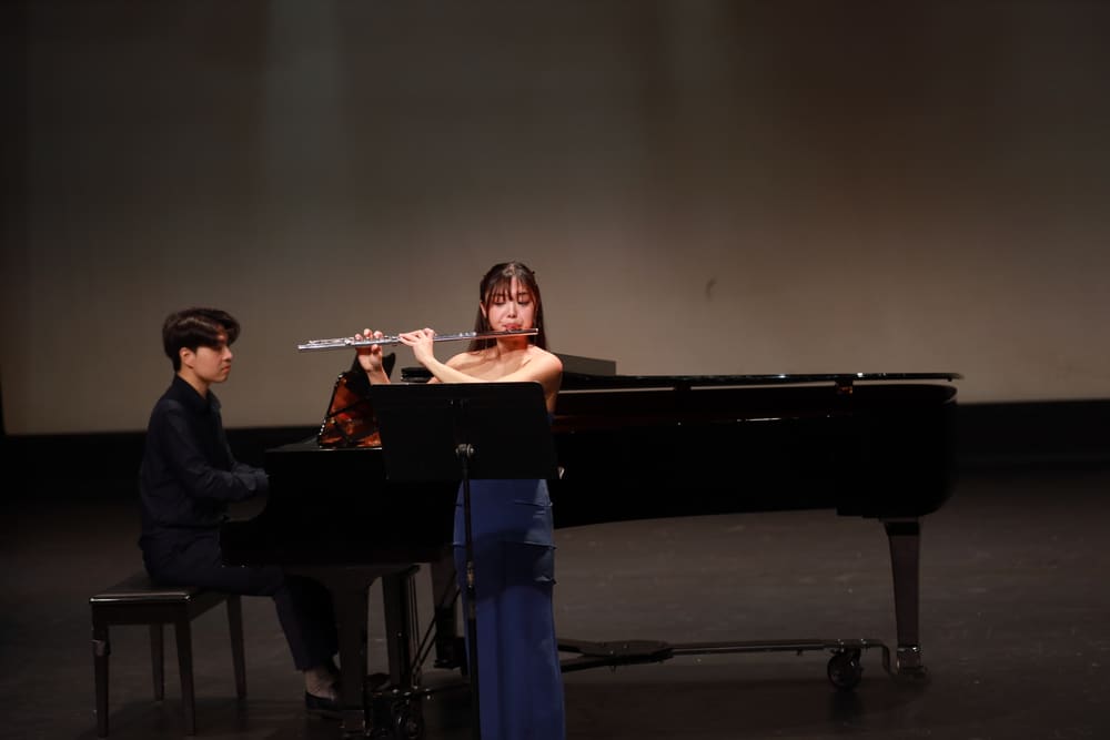 Monica playing the flute beside a pianist on a dark stage